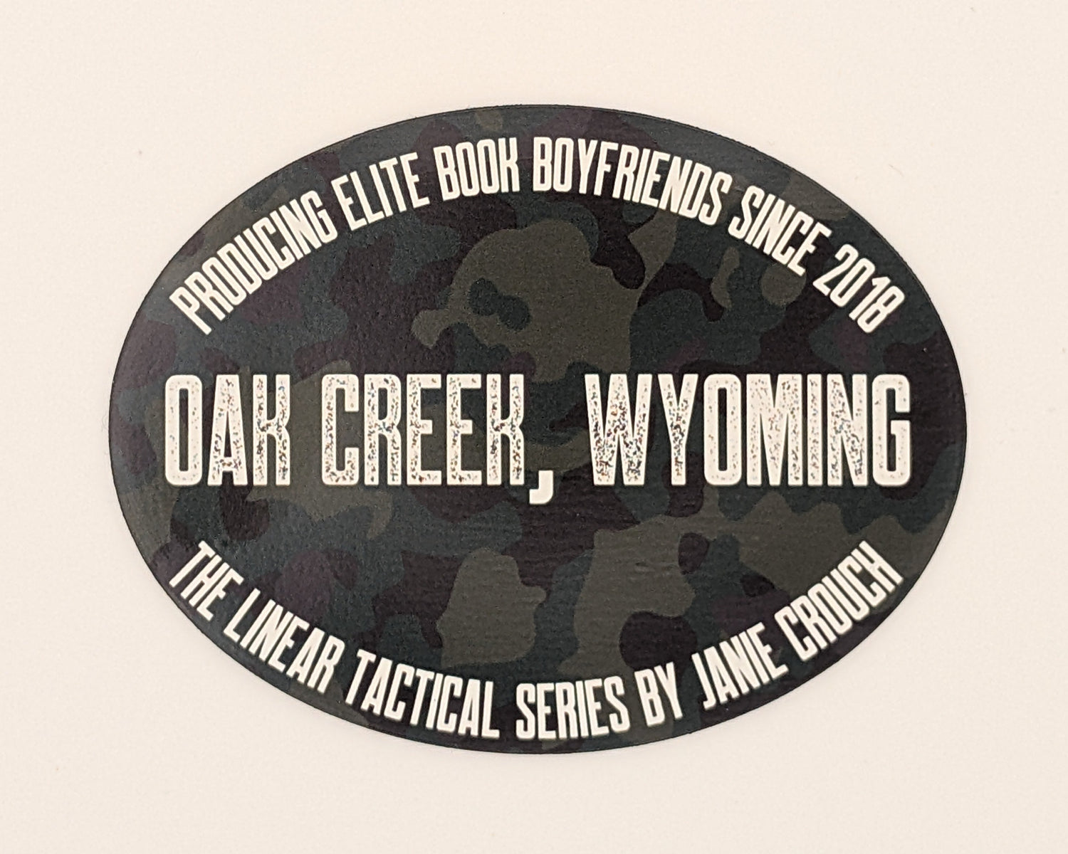 Dark camo oval sticker with white text noting that Oak Creek, Wyoming has been "producing elite book boyfriends since 2018"